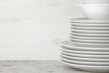 A stack of dishes. tableware on a light concrete background. dishes for serving the table. white plates and bowls in a stack. space for text - obrazy, fototapety, plakaty