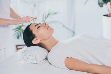 cropped shot of peaceful young woman with closed eyes receiving reiki treatment