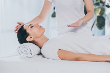 peaceful young woman receiving reiki healing treatment on head and chest