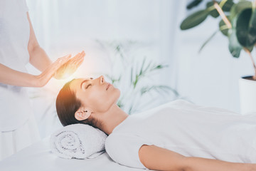 peaceful young woman with closed eyes receiving reiki treatment on head