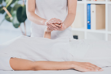 cropped shot of reiki healer holding female hand during session
