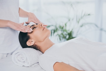 cropped shot of young woman with closed eyes receiving reiki treatment on face - obrazy, fototapety, plakaty