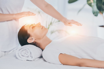 cropped shot of reiki healer doing therapy session to calm young woman with closed eyes - obrazy, fototapety, plakaty