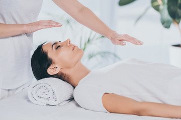 cropped shot of young woman with closed eyes receiving reiki treatment on head and chest