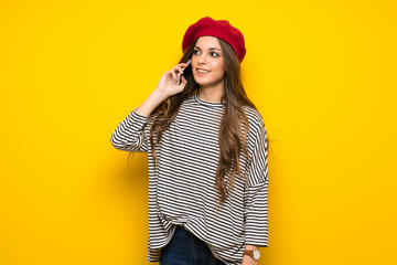 Girl with french style over yellow wall keeping a conversation with the mobile phone