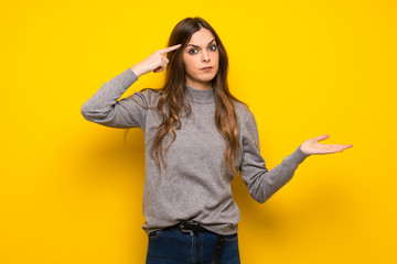 Young woman over yellow wall making the gesture of madness putting finger on the head