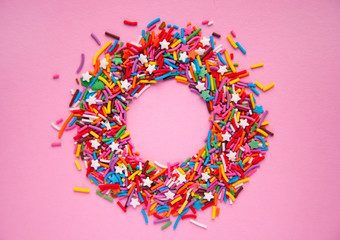 Circle frame from colorful sprinkles on pink background