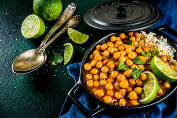 Vegan indian food, Sweet Potato and Chickpea curry, Chana Masala, with lime slices and spices on dark green stone table top ciew copy space