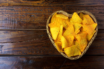 Nachos corn chips placed in basket with heart shape on wooden table, space for text. top view