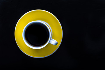 Yellow cup of coffee on a black background. Minimalism. Top view