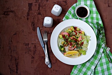 Green salad with avocado, baked salmon and dried tomatoes in a white plate on a gray concrete background. Top view.