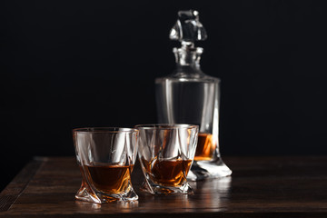 close-up view of glasses and bottle of whisky on dark wooden table isolated on black