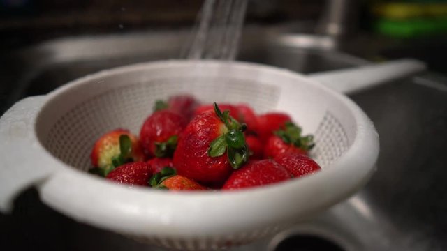 Washing strawberries close up in a strainer. Shot on Batis 25mm on a Sony A7iii.