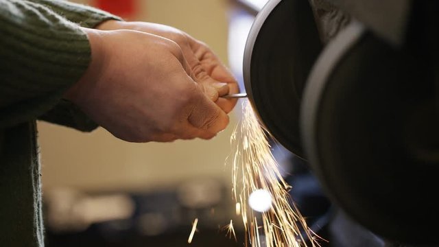 Locksmith smoothing the edges of a freshly cut key on a sanding belt
