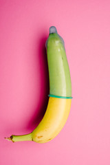 Banana with green condom in front of pink background