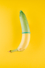 Banana with green condom in front of yellow background