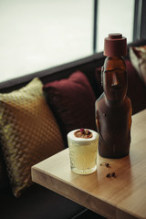 bronze statue and alcoholic cocktail decorated with dry orange on wooden table in restaurant