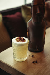 selective focus of bronze statue and alcoholic cocktail decorated with dry orange on wooden table in restaurant