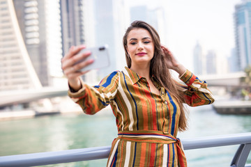 Young pretty woman taking selfie on the phone on Dubai marina background