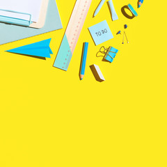 School desk with blue supplies on yellow background. Creative flat lay.	