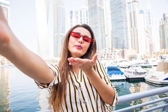 Young pretty woman tourist in sunglasses blow kiss on camera taking selfie photo in Dubai Marina in United Arab Emirates.