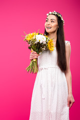happy young woman in white dress holding flower bouquet and looking away isolated on pink