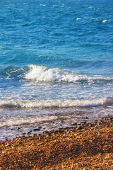 Waves on pebble beach on calm sunny day. Montenegro, Adriatic Sea