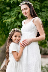 Fototapeta premium adorable happy child hugging pregnant mother and smiling at camera in park