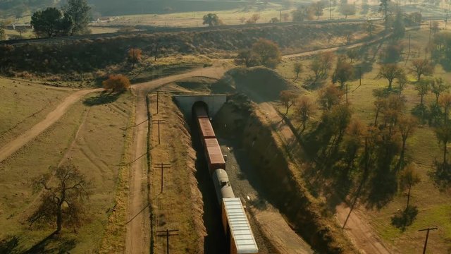 The aerial camera flies 125 feet above a train coming out from the western side of the rail loop tunnel. Camera then pans up and flies over and past the crisscross of the rail loop.