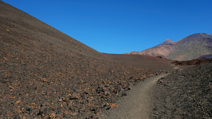 Path through the lunar landscape of Montaña Samara in Teide National Park, one of the most alien-like, volcanic land in Tenerife with views towards Pico del Teide, Pico Viejo, and Las Cuevas Negras