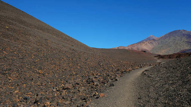 Path through the lunar landscape of Montaña Samara in Teide National Park, one of the most alien-like, volcanic land in Tenerife with views towards Pico del Teide, Pico Viejo, and Las Cuevas Negras
