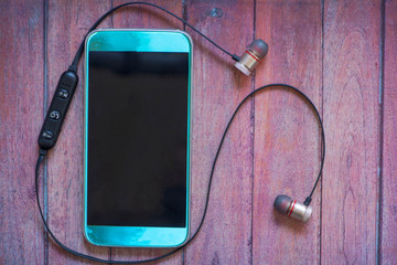 A blue mobile phone with bluetooth headphones on wood