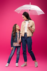 happy daughter and mother with umbrella holding hands and smiling each other on pink