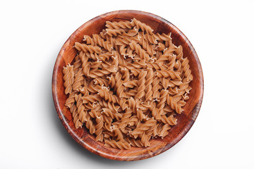 Raw brown pasta in wooden bowl. Food container isolated on white in studio. Cooking background.