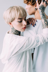 blonde woman with tattoos touching handsome boyfriend isolated on grey