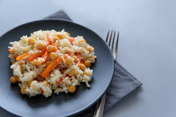 Tasty vegetarian pilaf with rice, carrot and chickpeas on gray wooden background. Copy space. Top view. Selective focus
