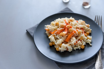 Tasty vegetarian pilaf with rice, carrot and chickpeas on gray wooden background. Copy space. Top view. Selective focus