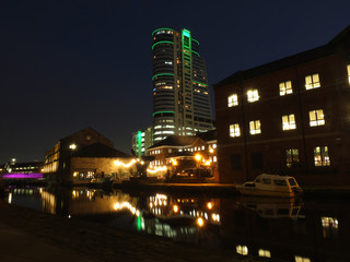 leeds canal wharf at night with brightly illuminated buildings and lock reflected in the water and glowing against a dark sky
