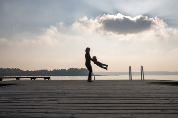 Mother spinning her toddler son on a wooden pier over the sea