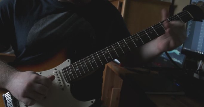 Skilled guitarist plays a fast solo on his electric guitar. Naturally light in a bedroom setting.