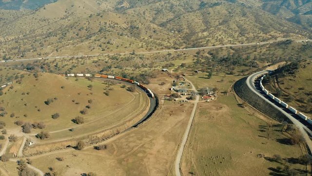 The aerial camera follows the end of an extremely long trail of railroad cars going around Cross Hill in the Tehachapi Railroad Loop from 300 feet above the ground.