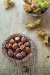 Top view photo composition of just harvested whole hazelnuts with shells in a plate of dried leaves on the rustic wooden board. Selective focus. 2