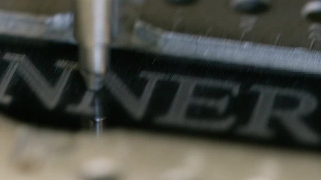 Camera pans across a CNC engraver shading text of the word WINNER