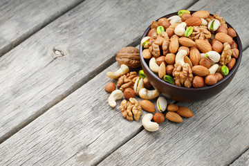 Wooden bowl with mixed nuts on a wooden gray background. Walnut, pistachios, almonds, hazelnuts and cashews, walnut.