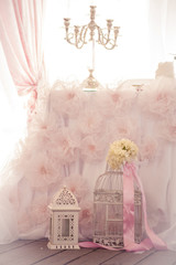 Part of the decor of the holiday table. Wedding day. Decorative white bird cage, candlestick. Decorated with flowers and pink ribbon