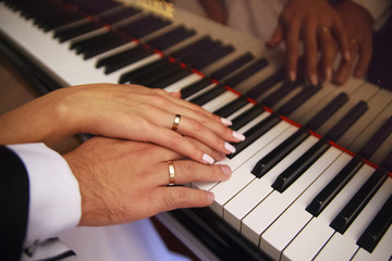 Obraz premium Two hands on the piano. Play. The piano keys. Wedding. A touch of hands. Wedding rings. Closeup