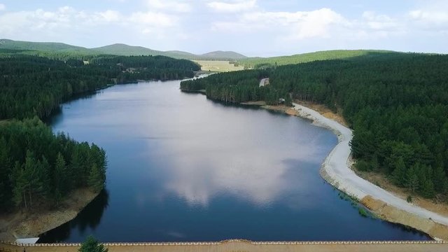 Aerial, drone shot, over a dam and a reflecting lake, towards forest and mountains, on a half cloudy, summer day, in Afyon, Afyonkarahisar region, Turkey