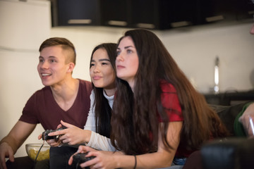 Company of young friends spending time together. A young woman holding a joystick