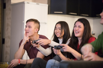 Company of young friends spending time together. Two young woman playing game using a joystick. Excitement