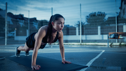 Beautiful Energetic Fitness Girl Doing Push Up Exercises. She is Doing a Workout in a Fenced Outdoor Basketball Court. Evening Shot After Rain in a Residential Neighborhood Area.